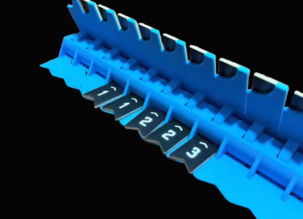 Bomb Busters Player Wire Stands. A close-up of a bright blue plastic component with multiple small dark gray numbered tabs or slots, shown against a solid black background.