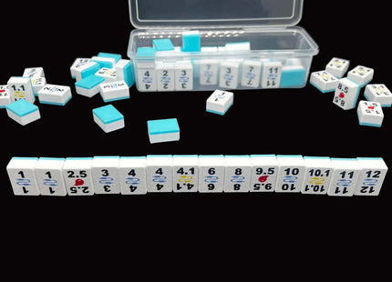 A set of Mahjong tiles arranged on a black background, with an open clear plastic storage case behind them. The tiles are mostly white with light blue sides and black printed numbers and symbols, with a few tiles showing red and yellow accents.