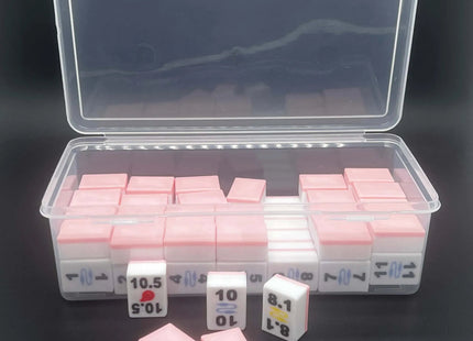 A clear plastic storage case containing multiple small pink-and-white rectangular blocks, with three of the blocks placed in front on a dark background.